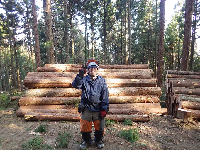 切り出された木材の前でポーズをとる従業員の写真